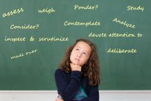 A schoolgirl in front of a blackboard considering all the synonyms for the word consider.